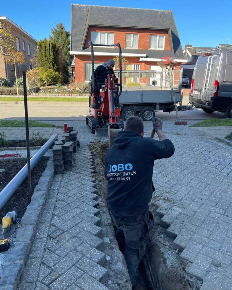 Techniekers van Jobo Ontstoppingen voeren rioleringswerken uit met een graafmachine en handmatige graafwerken in een oprit.
